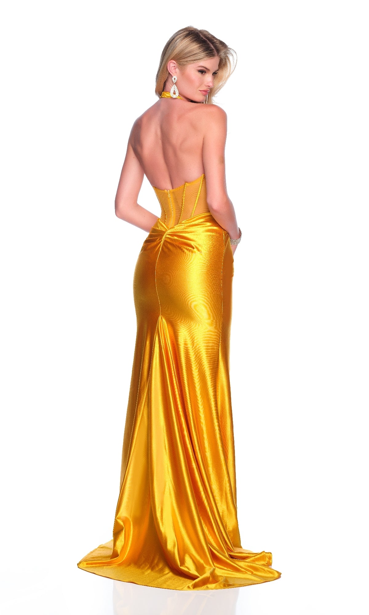 A woman stands against a white background, facing away, wearing the Dave & Johnny 12133 long yellow prom dress with a strapless sheer corset bodice and large drop earrings.